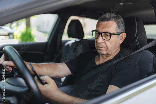 Senior in his 70s driving a car and using his mobile phone