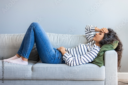 Full length young woman lying on sofa suffers from heartache cover face with hands crying feels desperate unhappy unwell having mental pain or serious health problems, beak up divorce abortion concept