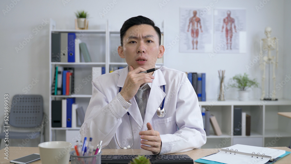 physician pointing to note with a pen is nodding while listening and spreading his hand as he is answering patient’s question at a remote appointment.