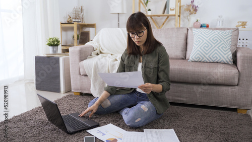 elegant woman worker checking detail on document and holding paper while sitting on carpet in bright home living room