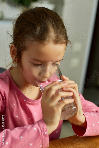 Close up of happy little girl drinking glass fresh water in kitchen