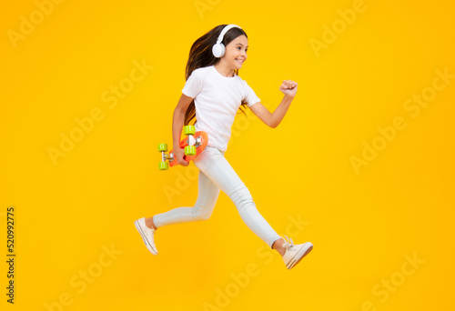 Teen girl 12, 13, 14 years old with skateboard over studio background. Jump and run. Cool modern teenager in stylish clothes. Teenagers lifestyle, casual youth culture. Excited teenager emotions.