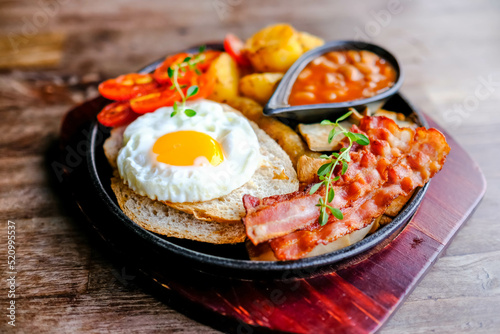 Delicious English breakfast with a fries egg, beans, bacon, and roasted potatoes.