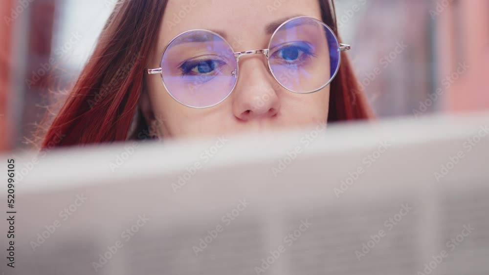Thoughtful young woman reading newspaper on street. Confused young female entrepreneur with long brown hair in formal clothes and eyeglasses standing on city street at reading newspaper Thoughtful young woman reading newspaper on street. Confused young female entrepreneur with long brown hair in formal clothes and eyeglasses standing on city street at reading newspaper
