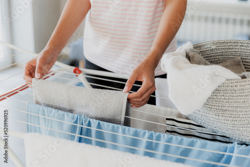 Woman hanging clean wet clothes laundry on drying rack at home laundry room