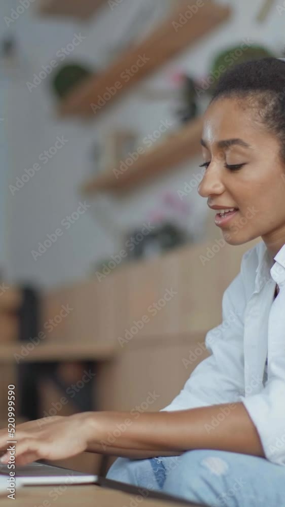vertical video of happy african american woman in headphones using laptop while working remotely in cafe vertical video of happy african american woman in headphones using laptop while working remotely in cafe