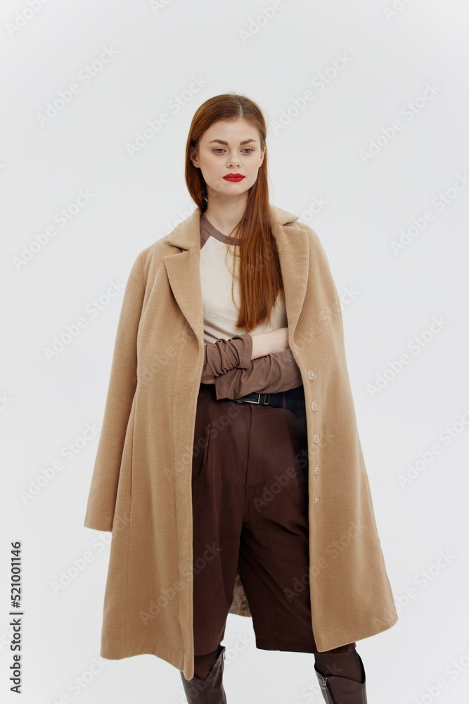 Fototapeta premium A lady with red lips in a beige coat on a white background poses for the new autumn-winter collection. Advertising for brands showrooms catalog of clothing for women