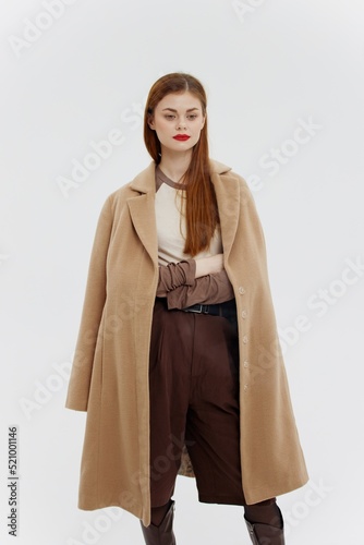 A lady with red lips in a beige coat on a white background poses for the new autumn-winter collection. Advertising for brands showrooms catalog of clothing for women © SHOTPRIME STUDIO