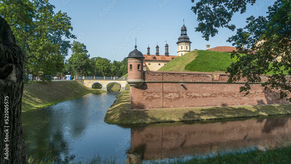 Moat of old castle. Moat with reflection in the water and trees. Sunny summer day. Palace, tower, corner towers and moat.