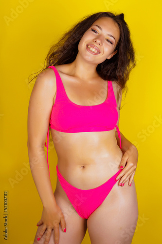 a beautiful Brazilian woman in a pink swimsuit poses on a yellow background