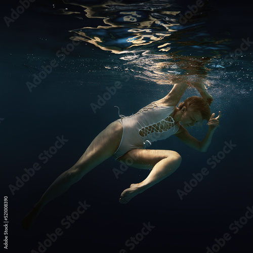 A woman in a white swimsuit underwater as if in weightlessness 