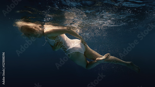 A woman in a white swimsuit underwater as if in weightlessness 