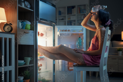 Woman cooling herself in front of the open fridge photo