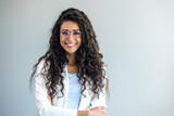 Portrait of young woman standing with hands on waist and looking at camera. Confident stylish latin girl standing against grey background. Happy young mixed race woman smiling isolated on gray wall