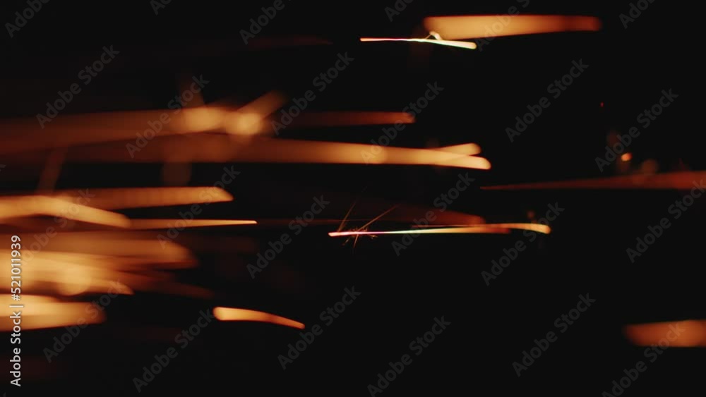 Glowing flow of metal welding sparks shining in dark, close-up. Golden sparkle light particles flying on black backdrop