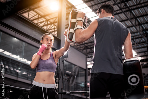 Young woman fitness wearing hand bandage ready to boxing throw a punch with trainer couple lover holding pads for boxing session ,they exercise for strong make muscle and good healthy lifestyle.