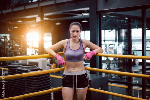 Young fitness woman with sitting on boxing ring .she under wearing boxing bandage safety in boxing exercise .She exercise for strong make muscle and good healthy lifestyle.