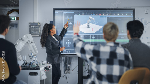 Caucasian Student Girl Raise Her Hand and Asking Teacher Standing Near the Big Screen. Teenagers Studying Robotic Arm at the Lesson In Modern University of Technology. Machine Learning Concept