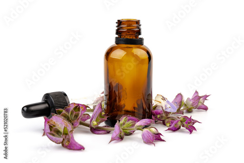 A bottle of essential oil with fresh blooming clary sage twigs on white background.