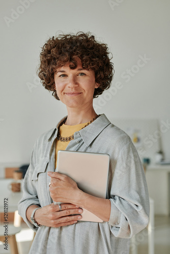 Portrait of young businesswoman with curly hair holding tablet pc and working at office