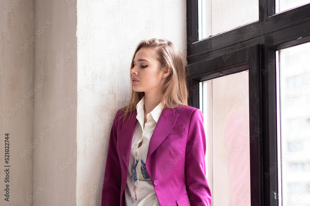 portrait of a young girl with long blonde hair in a purple suit next to the window with large glass portrait of a young girl with long blonde hair in a purple suit next to the window with large glass
