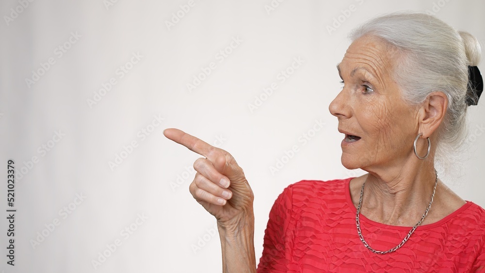 Portrait of elderly mature woman smiling showing area to side, giving thumbs up isolated on solid white background in studio. Portrait of elderly mature woman smiling showing area to side, giving thumbs up isolated on solid white background in studio.