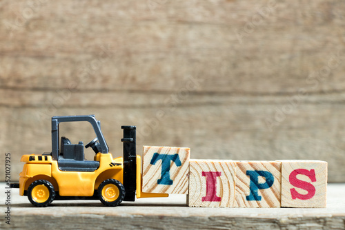 Toy yellow forklift hold letter block t to complete word tips on wood background photo