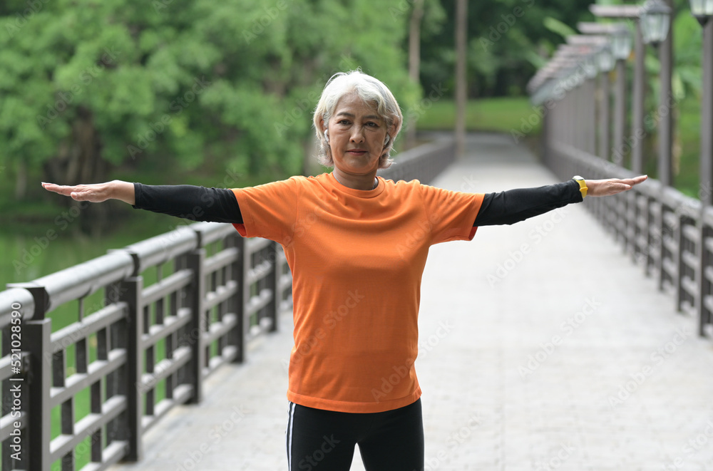 A retired Asian woman wearing an orange T-shirt is exercising outdoors, running, lifting dumbbells, stretching. A retired Asian woman wearing an orange T-shirt is exercising outdoors, running, lifting dumbbells, stretching.