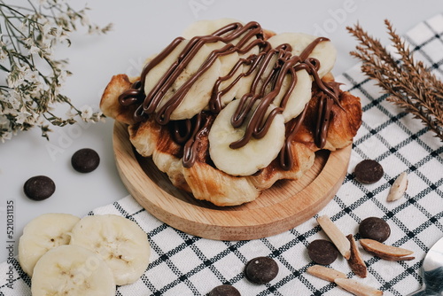 Croffle, Croissant Waffle Korea pastry. Croffle with different sweet topping banana slice and chocolate sauce served in wooden plate. Selective focus.