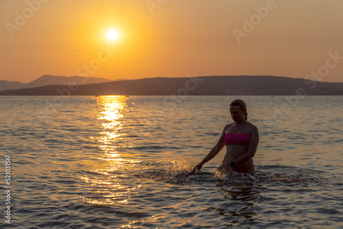 A girl is standing in the sea during sunset, the Adriatic Sea in Croatia © Goran