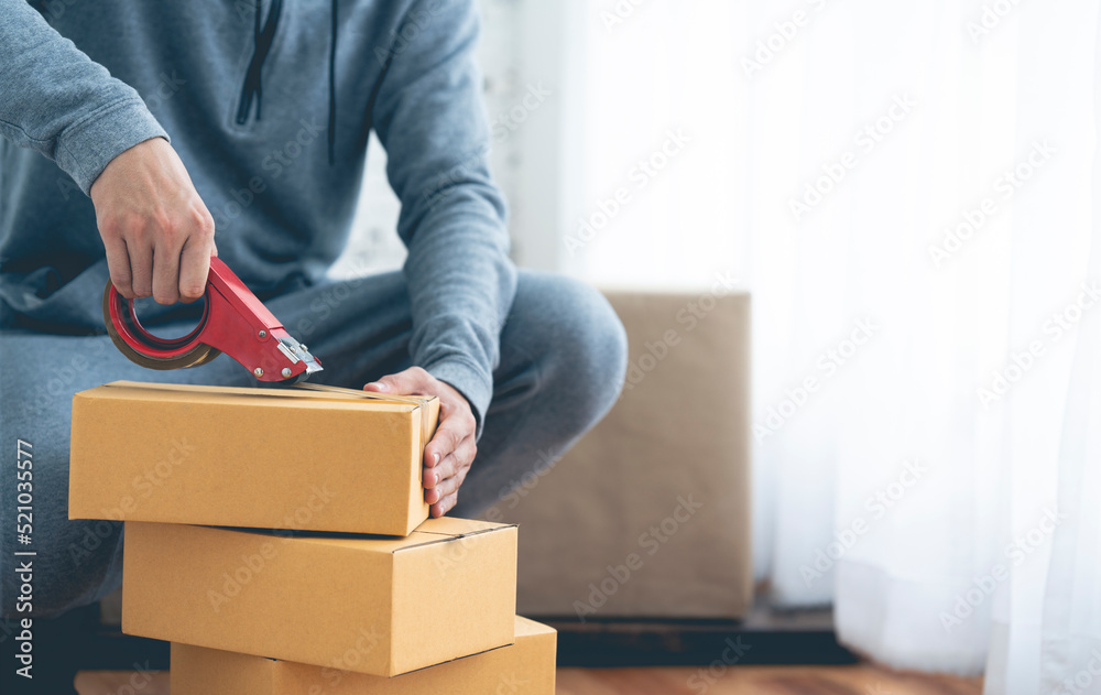 Detail of packing cardboard boxes while moving house. Young man packing box, indoors young male warehouse worker packing boxes for shipment. Detail of packing cardboard boxes while moving house. Young man packing box, indoors young male warehouse worker packing boxes for shipment.