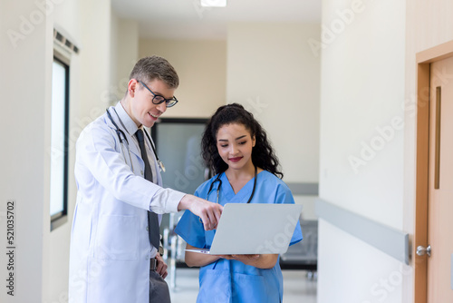 Clinicians in uniform standing and looking of computer monitor, discussing medical document and consulting. Doctor and nurse working on laptop in medical office. Professional medical work with Laptop
