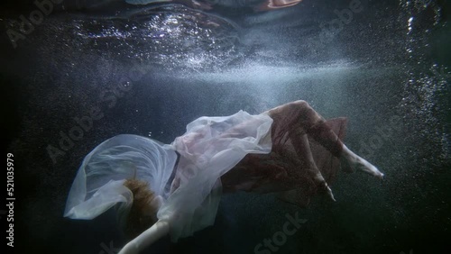 a red-haired woman in pink and white translucent fabrics hovers horizontally under the surface of dark water. the general plan