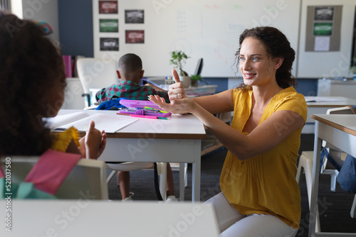 Smiling caucasian young female teacher talking to african american girl in sign language photo