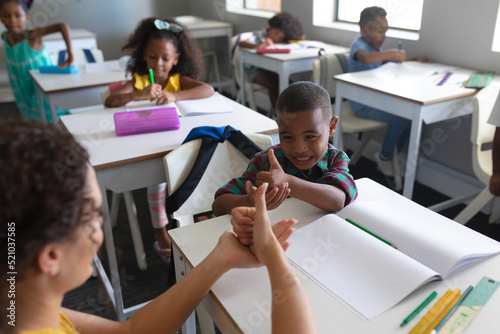 Young caucasian female teacher teaching sign language to happy african american boy in class