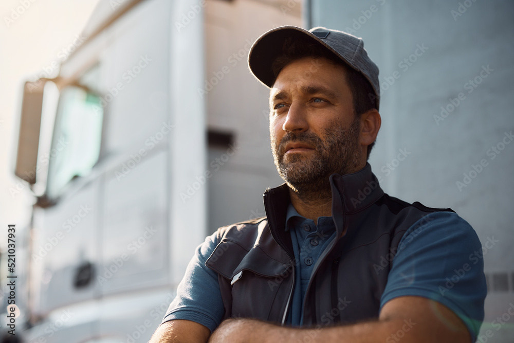 Obraz premium Pensive truck driver in front of his vehicle looking away,