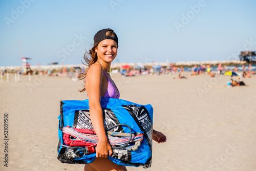 Beautiful woman kitesurfer prepares the kite on the beach and wearing kitesurfing equipment - concept of sporty woman and summer sport activity