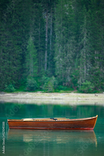 (Selective focus) Stunning view of a wooden boat floating on the Lake Braies (Lago di Braies) with a defocused forest in the distance. Lago di Braies is an alpine lake in the Dolomites, Italy