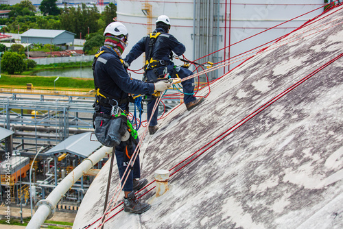 Male two worker inspection wearing safety first harness rope safety line working at a high place on tank roof spherical