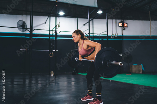 Caucasian fit girl with muscular body exercising and lifting barbell equipment during workout training in sportive studio, strong female with power have heavy practice in gym - endurance and effort