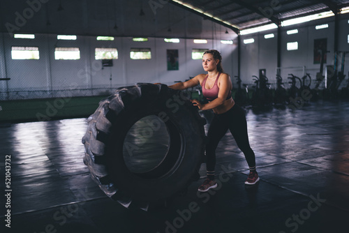 Caucaisan fit girl in sportive tracksuit using tire for weightlifting workout in gym class studio - endurance and effort with dedication, strong female athlete training during intensive crossfit