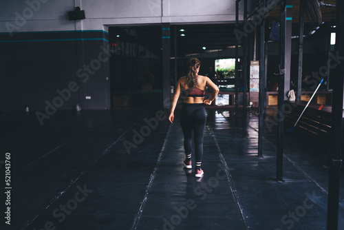 Sport and cardio training idea for keeping healthy lifestyle, back view of muscular female bodybuilder dressed in stylish tracksuit getting ready for pilates exercising in modern gym hall