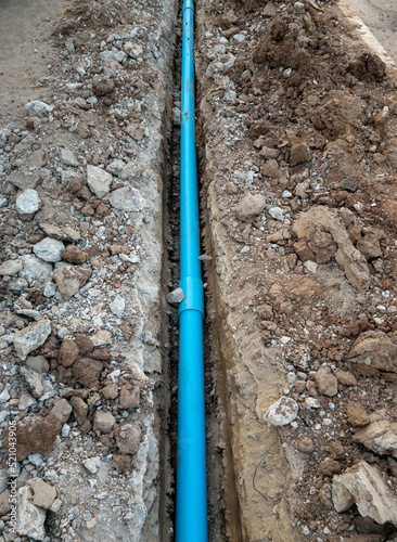 The new PVC pipe is laying in the trench near the asphalt road.
