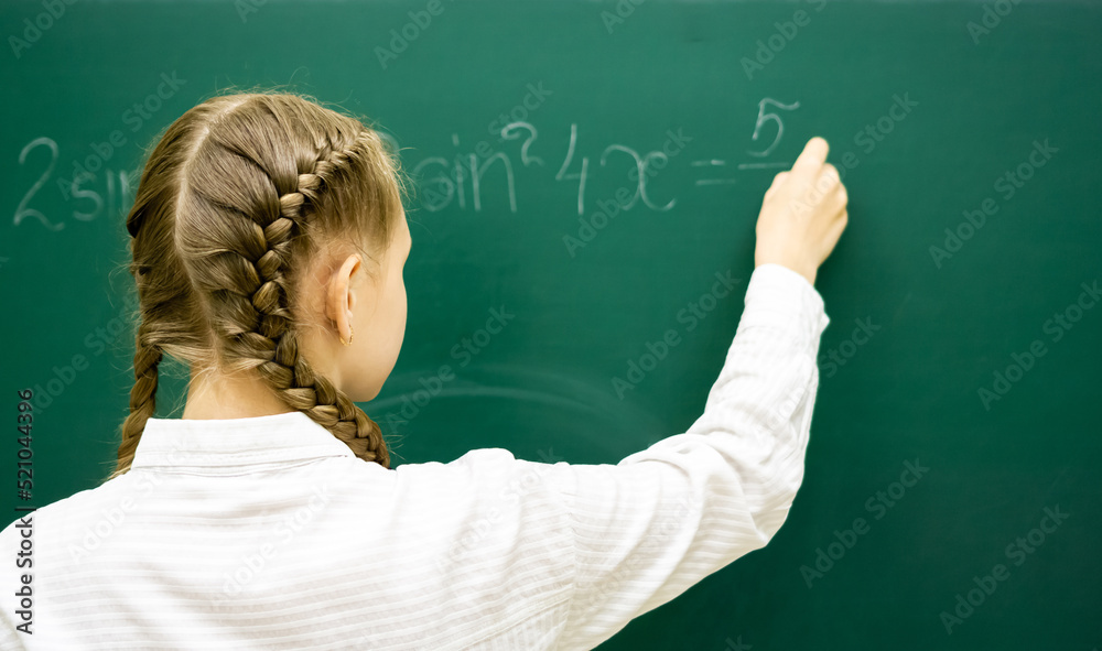 Female student teenager at a math lesson writing in chalk on a blackboard. Education, adolescence, high schoo. High quality photo