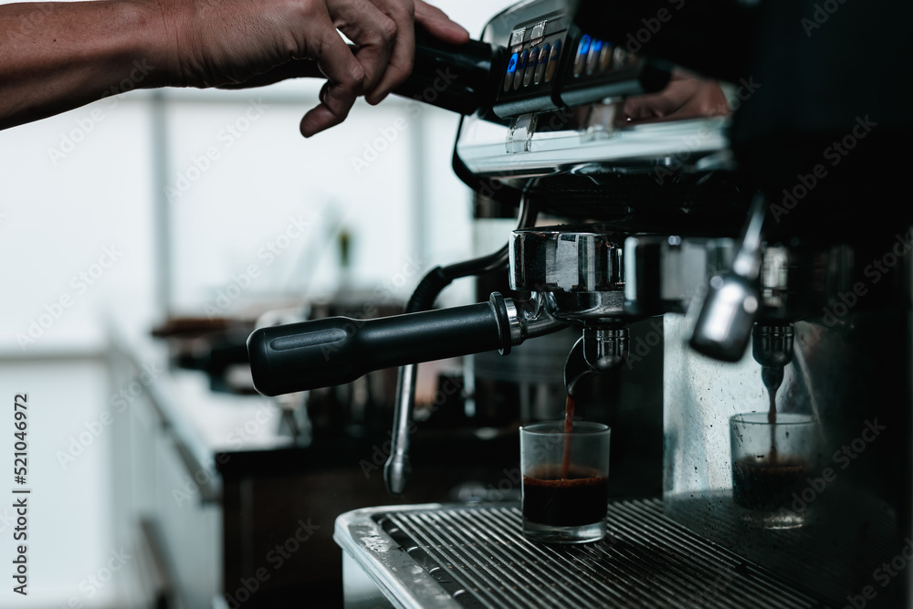 asian man bartender mixing and pouring coffee into cup from coffee machine at counter in small coffee shop