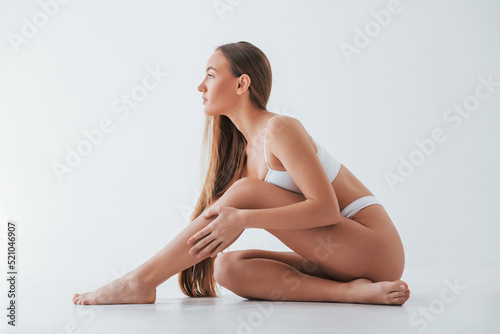 Beautiful model sitting on the floor. Woman in underwear with slim body type is posing in the studio