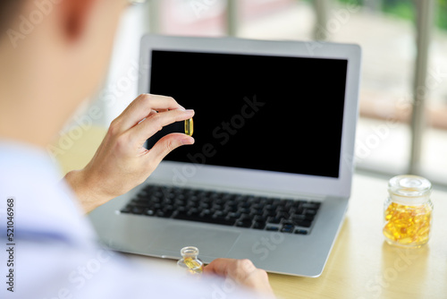 close up and silective focus rear viev doctor hands holding Omega-3 pills  and laptop computor on the table in office , healthy food supplements concept, photo