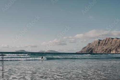 joven haciendo surf en una preciosa playa con acantilados al fondo