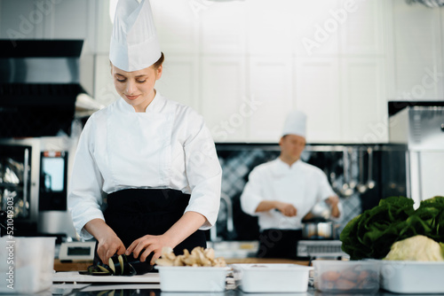 Professional restaurant kitchen, woman chef cuts zucchini