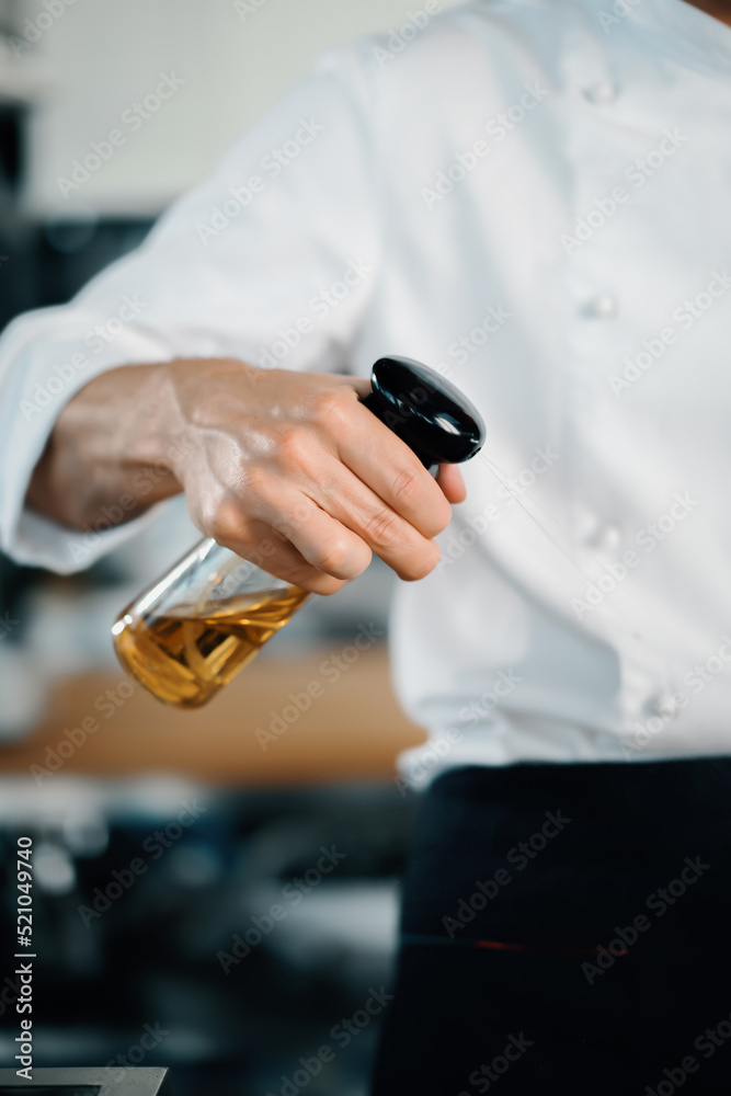 Obraz premium Professional restaurant kitchen, male chef splashes oil on mushrooms. Cooking delicious food in a restaurant.